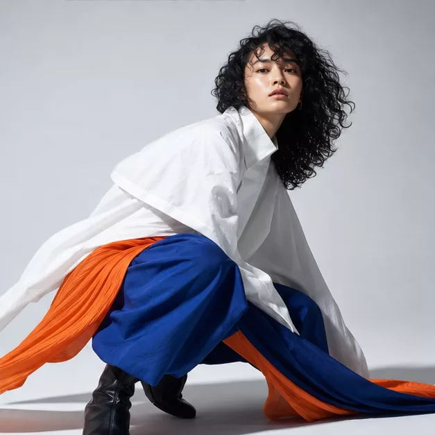 Crouching model in a white shirt over cobalt and orange fabric.