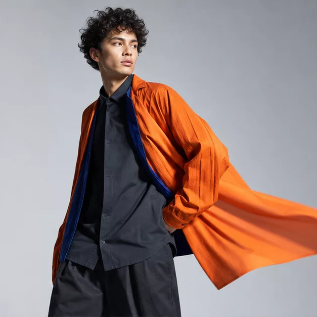 Model in a flowing signal-orange coat with a cobalt lining, mid-turn.
